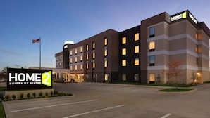 Ein modernes Hotel mit einem Schild, auf dem 'HOME 2 Suites by Hilton' steht, und einer Fahnenstange mit der amerikanischen Flagge.