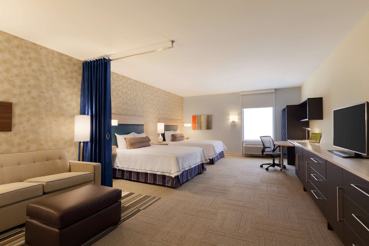 Une chambre d’hôtel avec deux lits, un canapé, un bureau, une télévision et une fenêtre avec des rideaux.