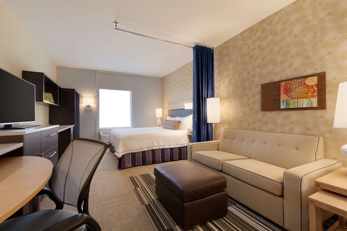 Une chambre d’hôtel comprenant un lit, un canapé, un bureau avec une chaise, une télévision et une fenêtre avec des rideaux.