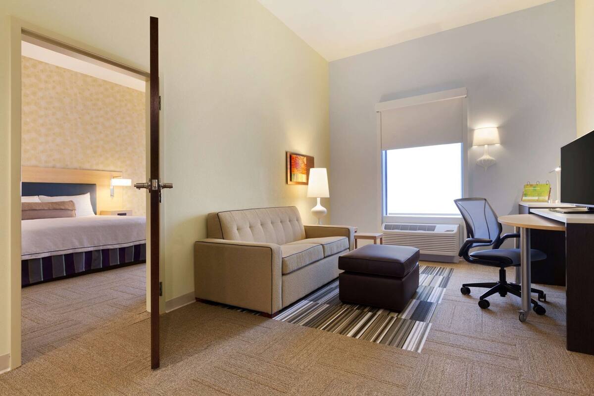 A hotel room with a bed, a sofa, a desk, a chair, and a window.