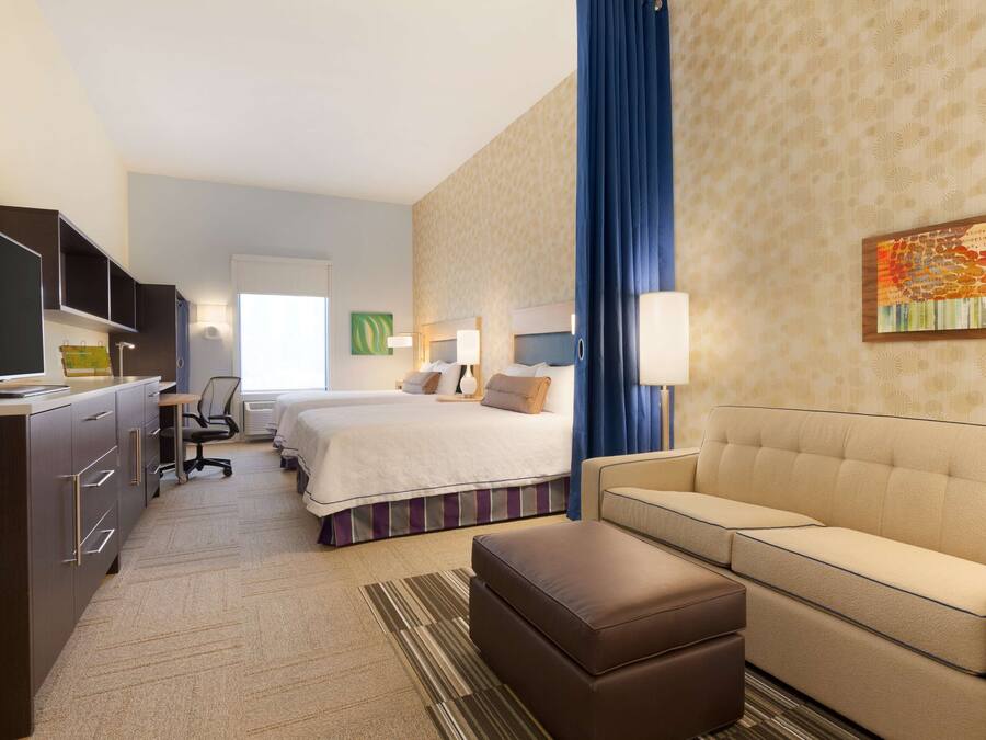 A hotel room with a bed, a sofa, a desk with a computer, a chair, and a TV.