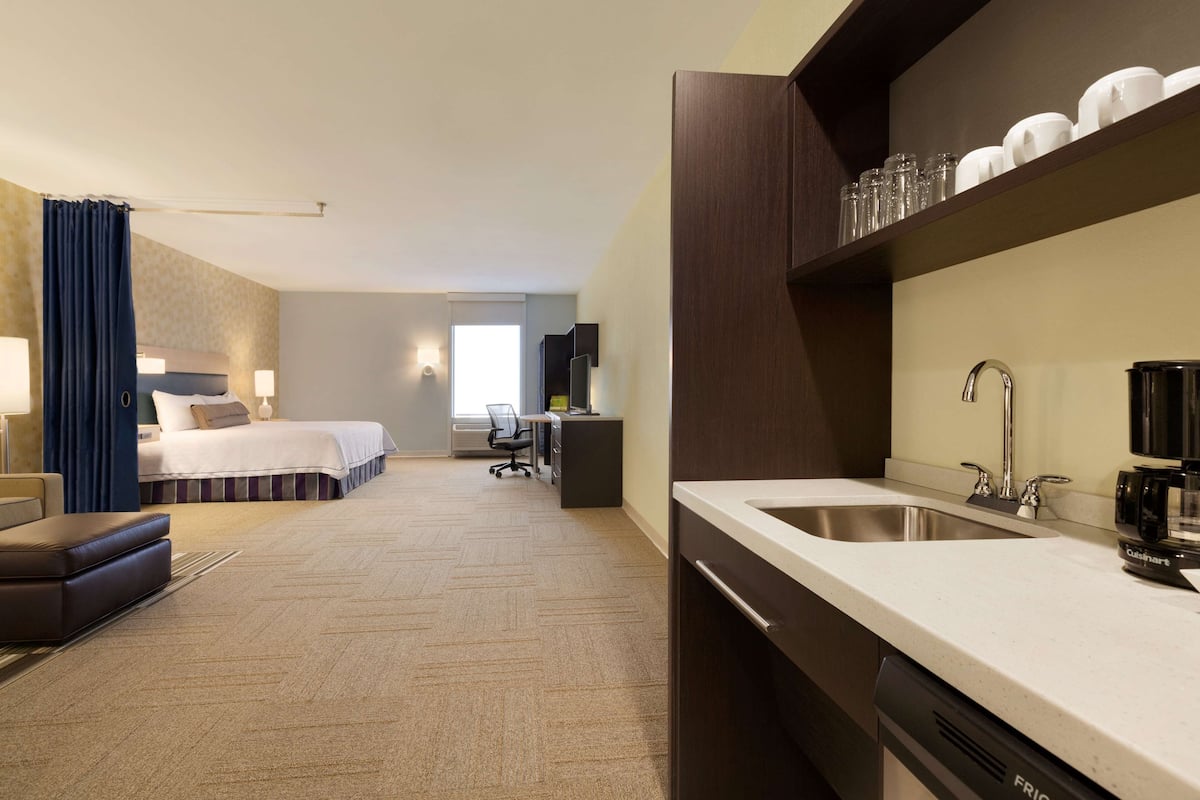 Une chambre d’hôtel comprenant un lit, un bureau, une chaise, un canapé, une machine à café, un lavabo et un miroir.