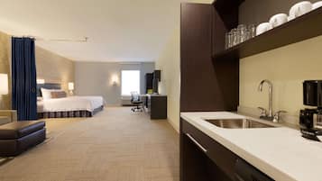 A hotel room with a bed, a desk, a chair, a sofa, a coffee machine, a sink, and a mirror.