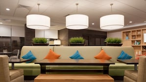Ein moderner Lounge-Bereich mit einer Couch, Sesseln, einem Holztisch und Pendelleuchten.