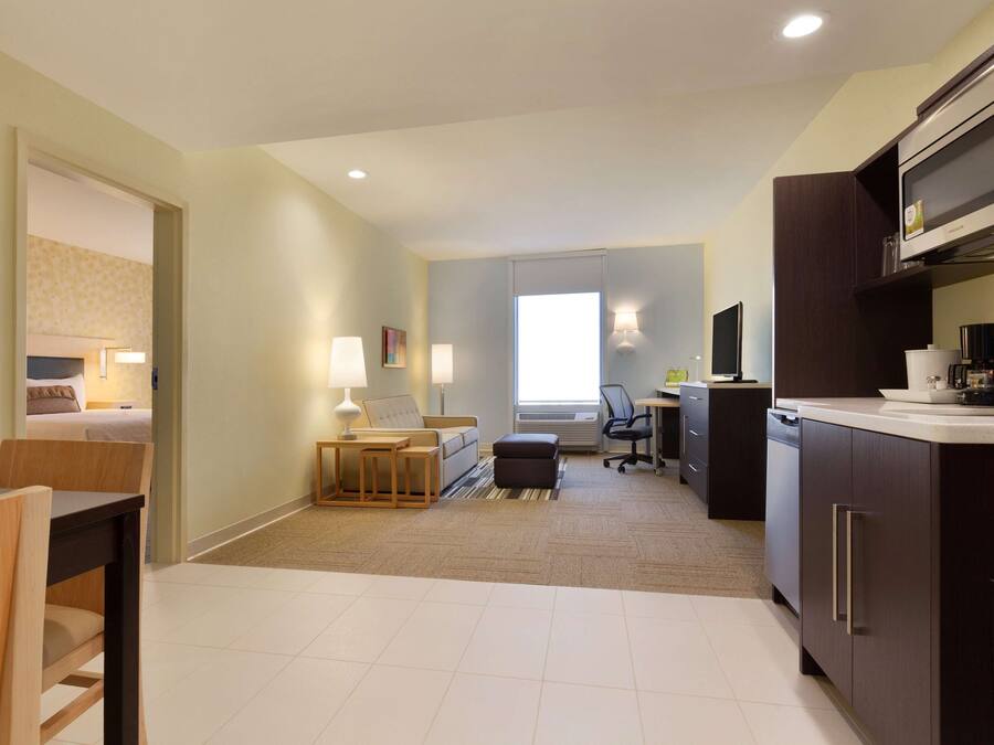 A modern hotel room with a kitchenette, a dining area, and a living space.