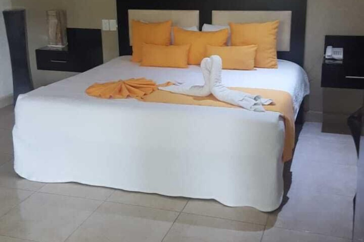 A neatly made bed with white and orange bedding, a headboard, and a ceiling fan above.