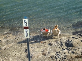 A bus stop sign on a rocky beach with two people sitting at a table.