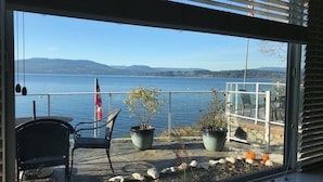 A balcony with a view of a lake and mountains, featuring potted plants, a chair, and a flag. - Inlet Beach House B&B (Sidney)