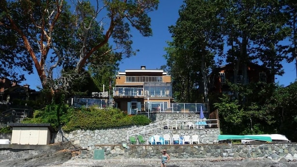 A waterfront property with a stone staircase leading to a balcony, surrounded by trees and a clear sky. - Inlet Beach House B&B (Sidney)