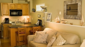 A cozy kitchen with wooden cabinets, a microwave, and a coffee maker. There's a dining area with a table and chairs. - Inlet Beach House B&B (Sidney)