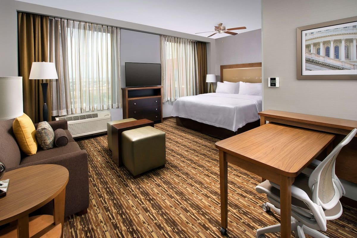 Habitación de hotel con cama, escritorio, sofá, televisor y ventilador de techo.