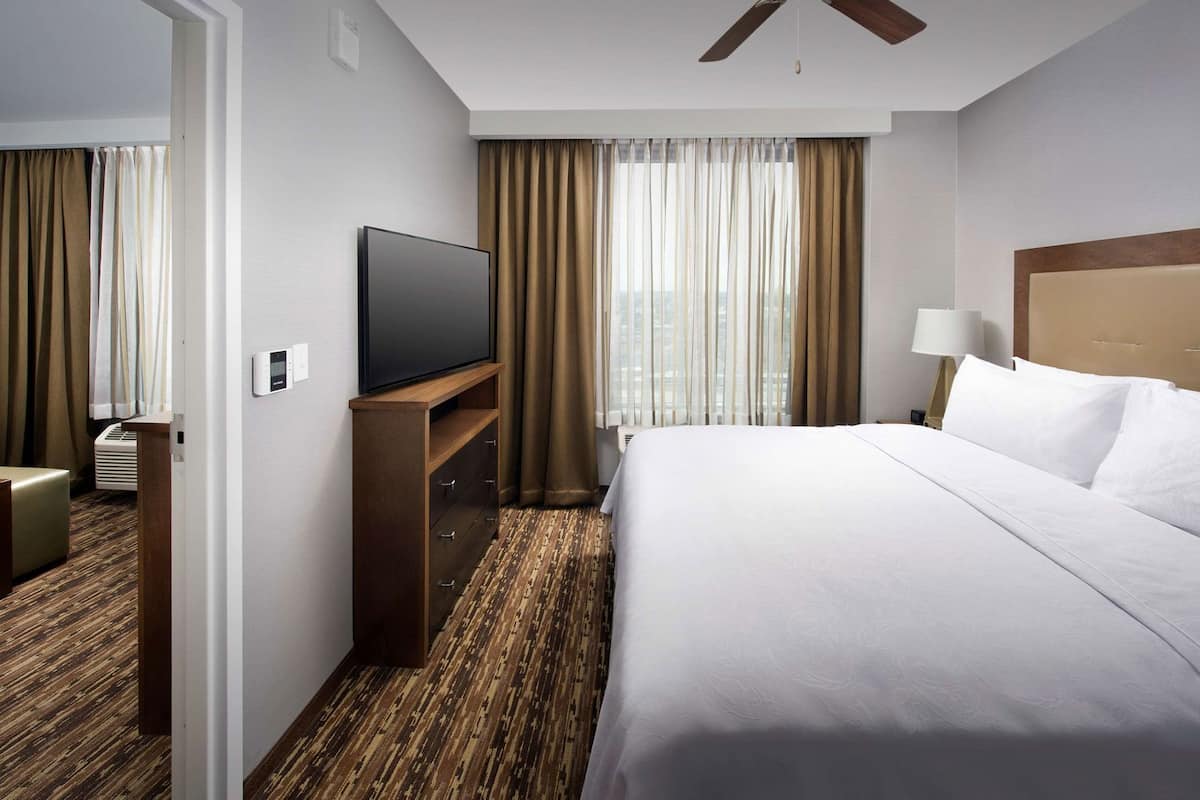 Habitación de hotel con cama, televisión, escritorio y ventana con cortinas.