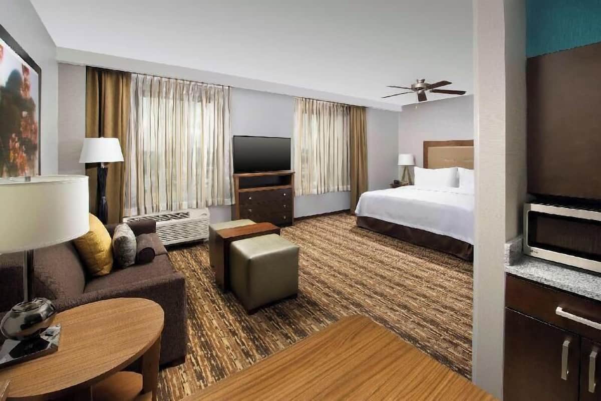 Una habitación de hotel con cama, televisor, escritorio con lámpara, sofá y ventilador de techo.