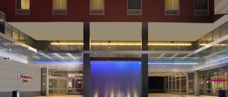 A hotel lobby with a large water feature, glass railings, and a sign for Hampton Inn.