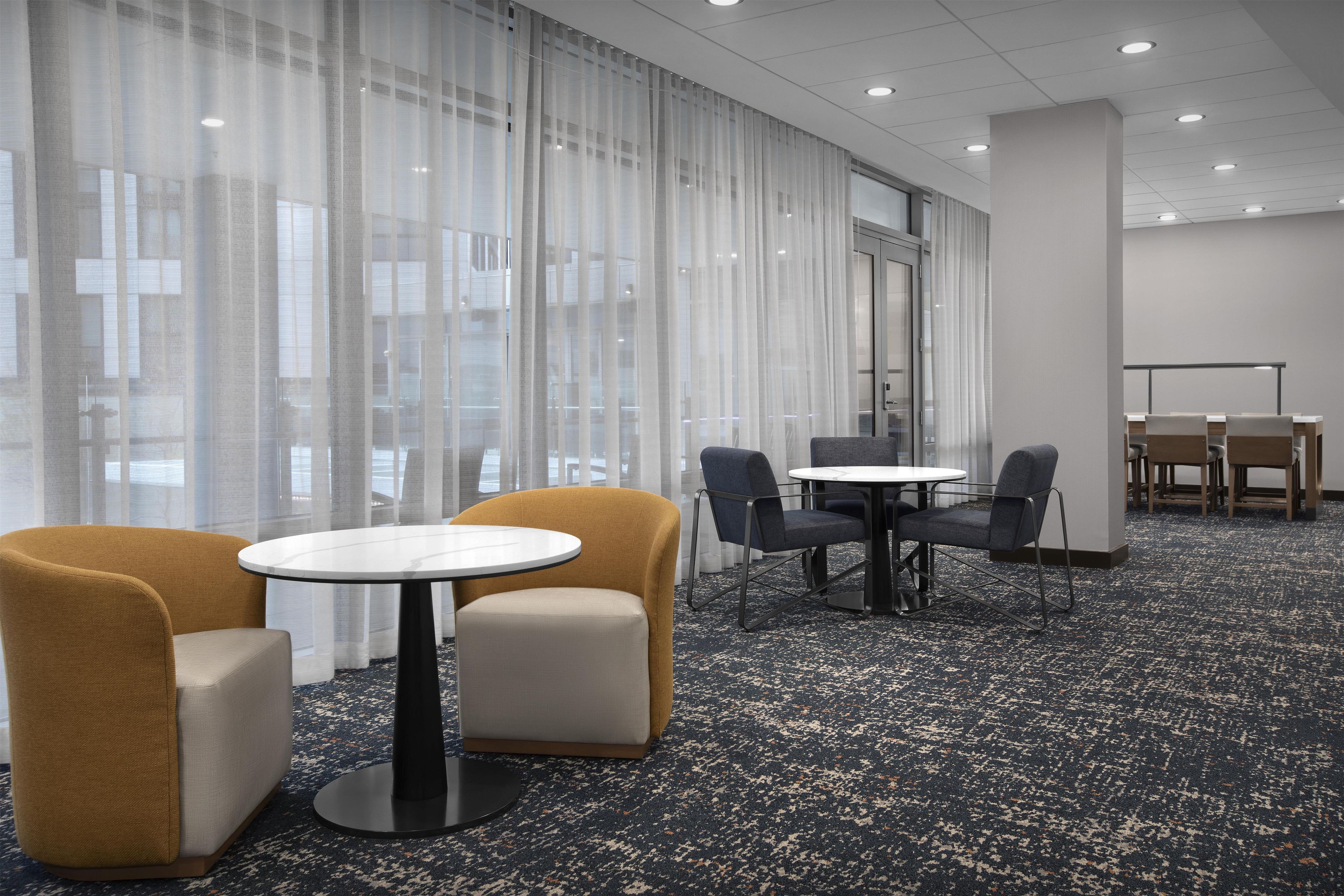 Una habitación de hotel con un ventanal grande, una mesa redonda, dos sillones y una pequeña mesa rectangular.