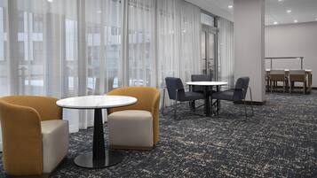 Una habitación de hotel con un ventanal grande, una mesa redonda, dos sillones y una pequeña mesa rectangular.
