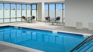 Ein Schwimmbecken mit klarem, blauen Wasser, umgeben von einer gefliesten Terrasse und großen Fenstern mit Blick auf eine Kuppel und Stadtlandschaft.