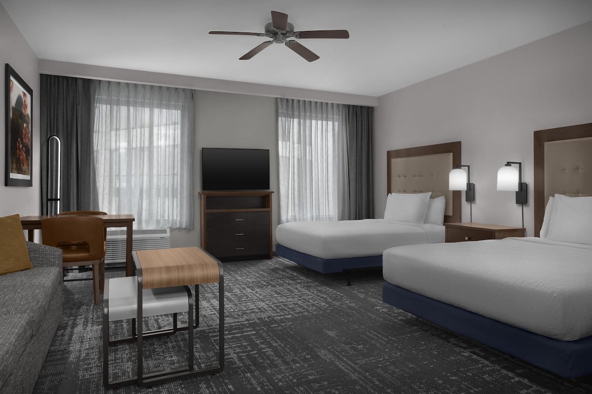 Una habitación de hotel con dos camas, un escritorio, una silla, un televisor y un ventilador de techo.