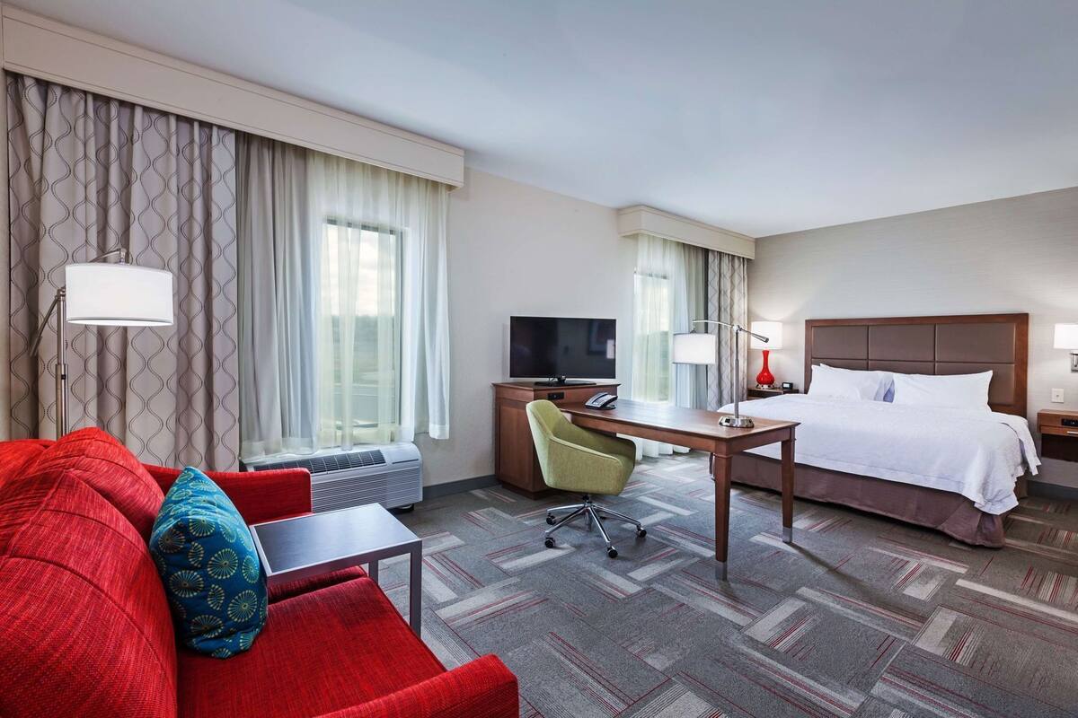 A hotel room with a bed, a desk with a chair, a TV, and a red sofa.