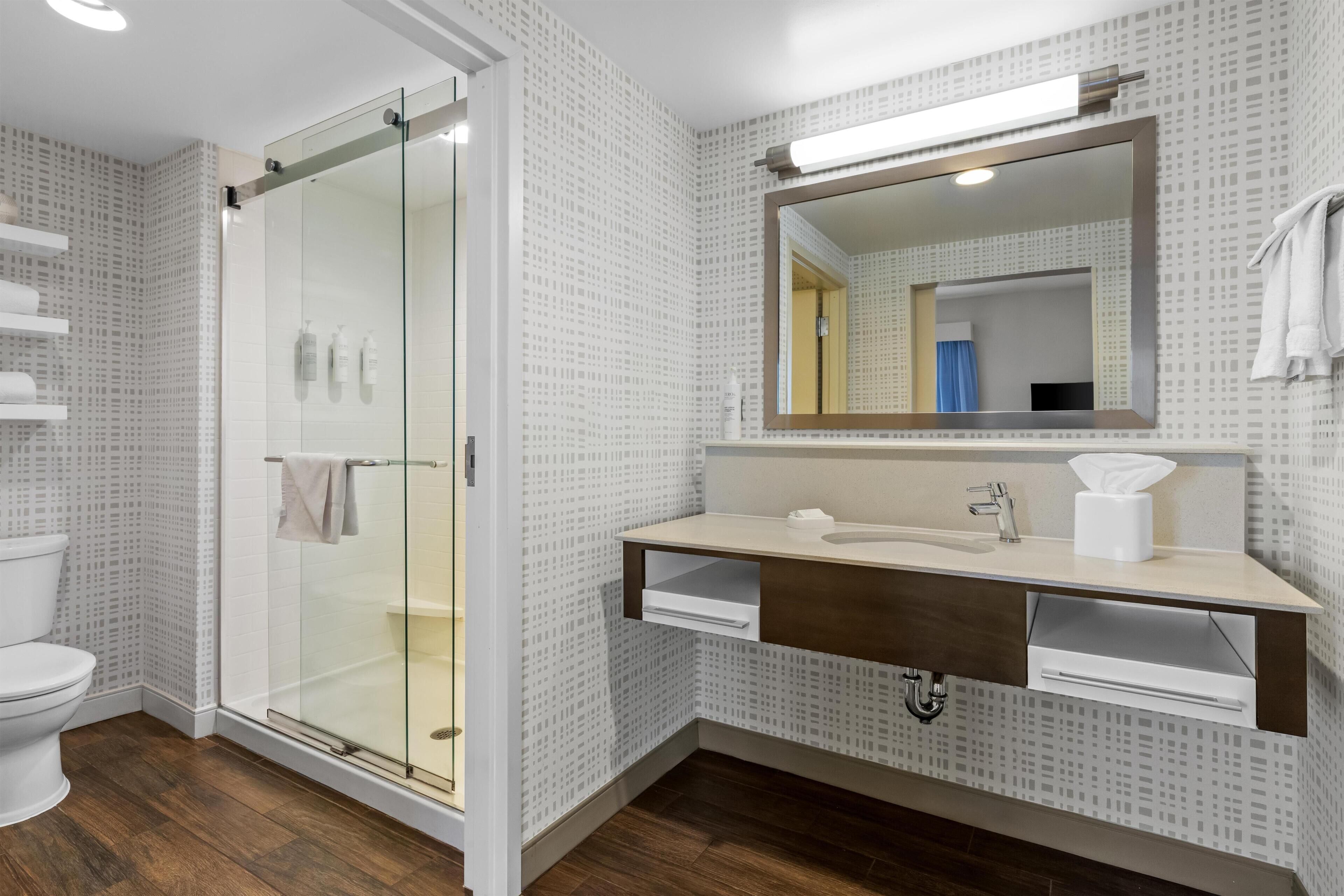 Ein modernes Badezimmer mit einer Duschkabine aus Glas, einer weißen Toilette, einem Waschbecken mit Spiegel und Wandfliesen mit Muster.