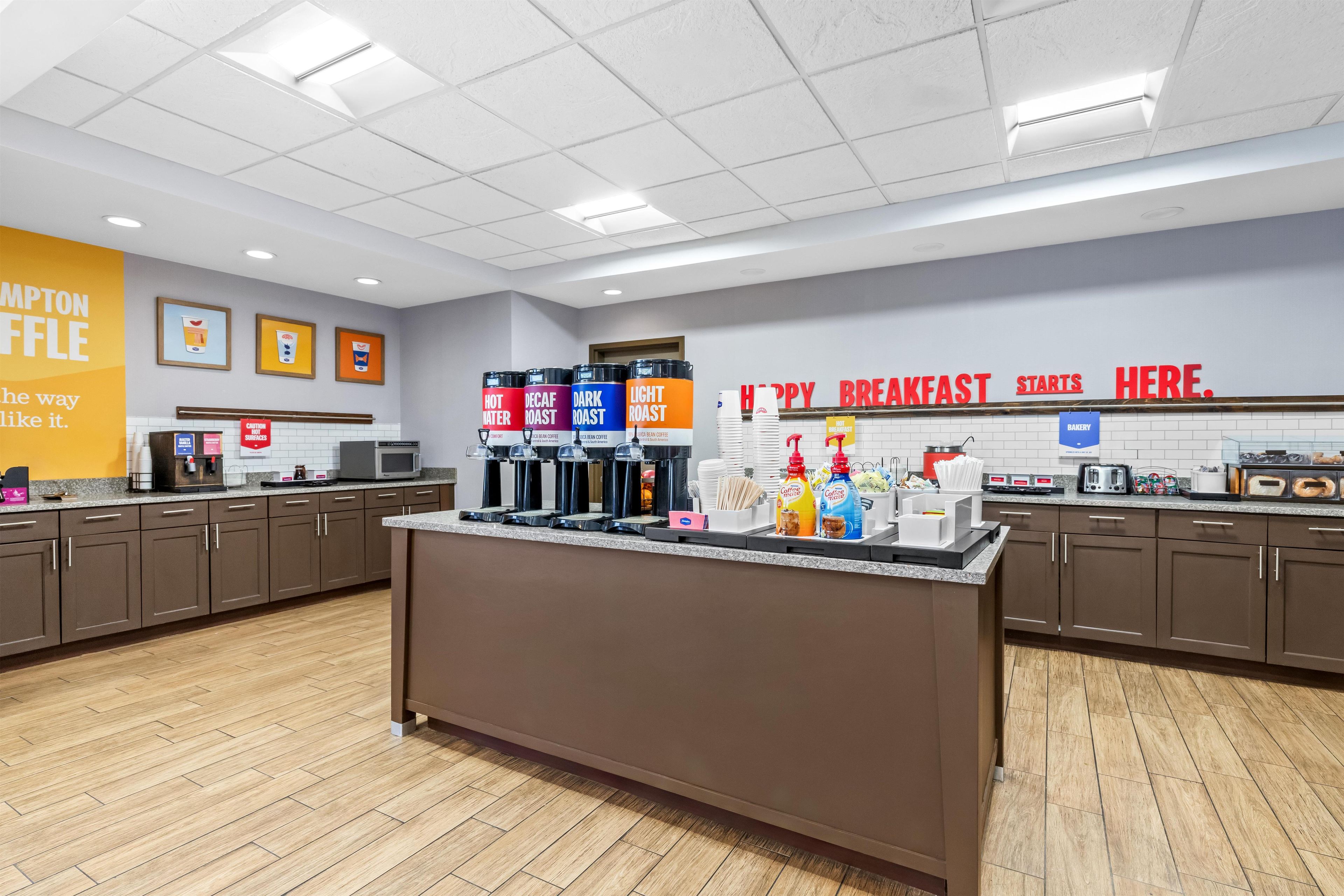A breakfast area with a counter, coffee machines, and a sign indicating the start of breakfast.