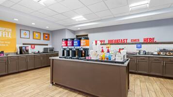 A breakfast area with a counter, coffee machines, and a sign indicating the start of breakfast.