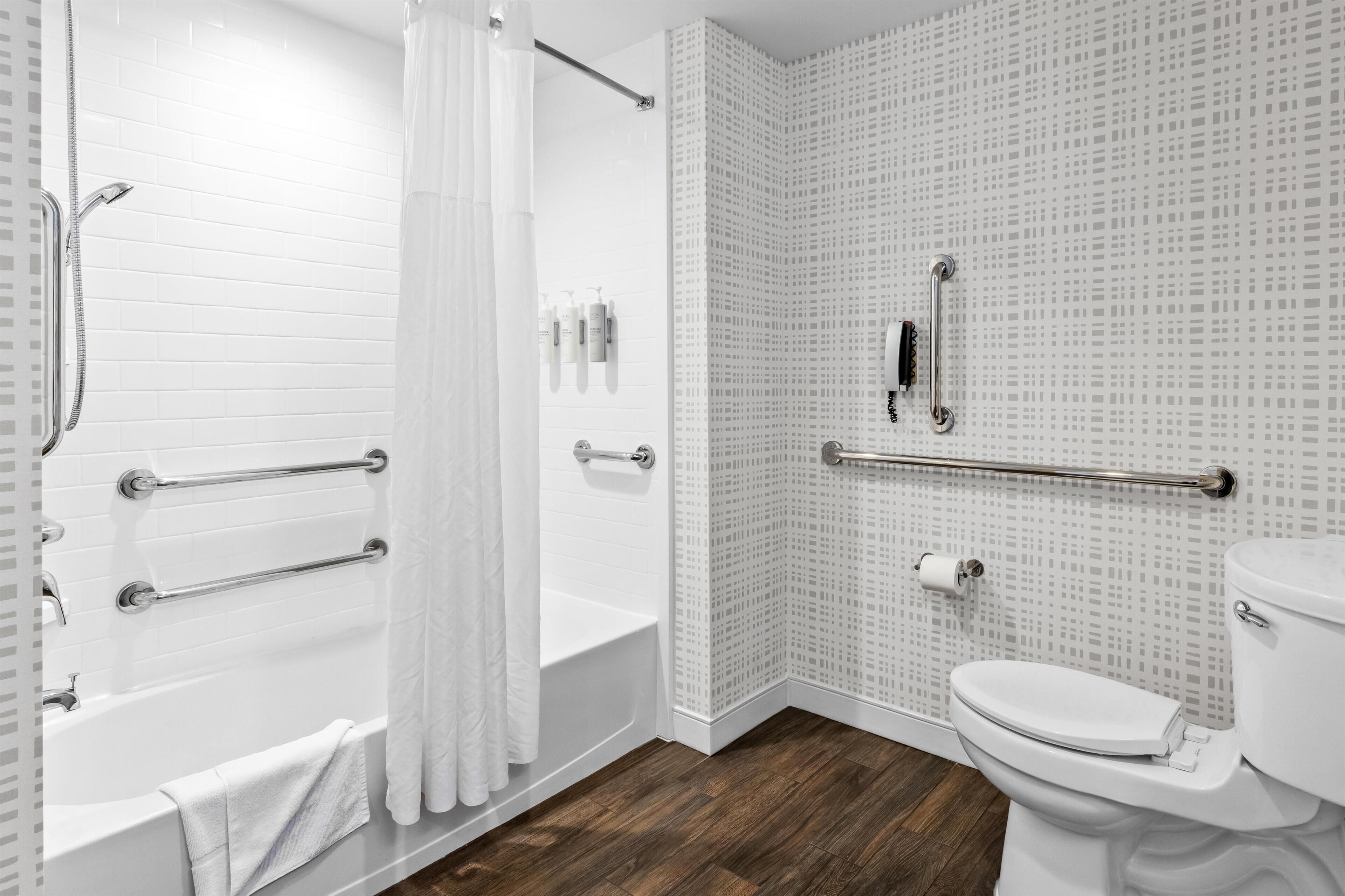 Une salle de bain équipée d’une baignoire, d’une douche, de toilettes et de barres d’appui.