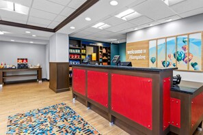 A hotel reception area with a red counter, a coffee station, and a wall with a 'Welcome to Hampton' sign. - Hampton Inn & Suites Claremore (Claremore)