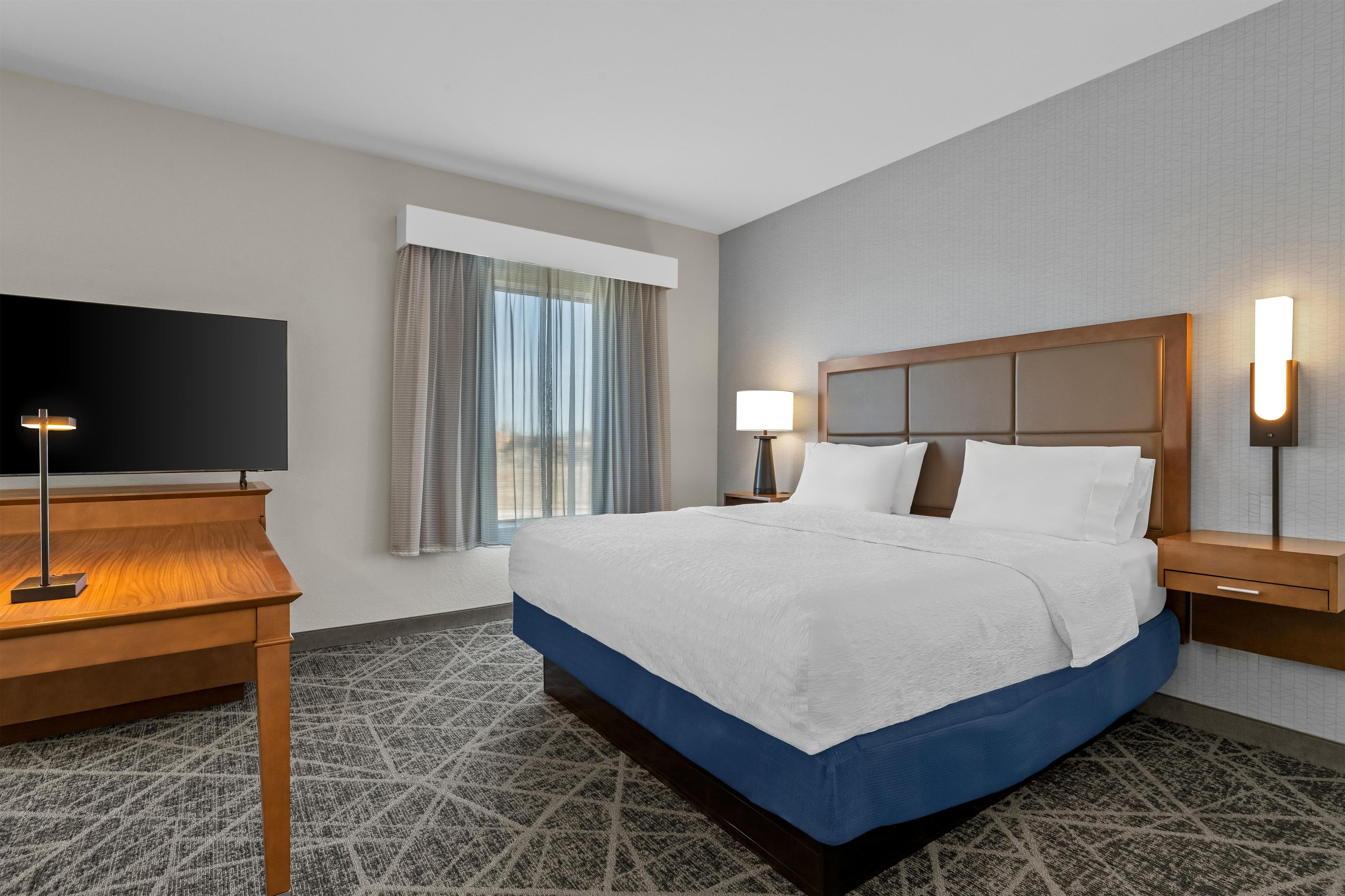 Habitación de hotel con una cama grande, un escritorio con televisor y una ventana con cortinas.