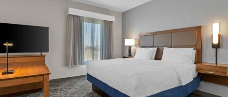 Habitación de hotel con una cama grande, un escritorio con televisor y una ventana con cortinas.