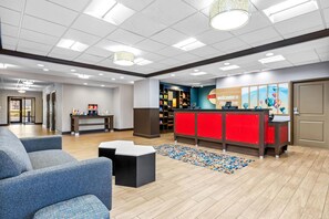 A hotel reception area with a red counter, seating, and a patterned rug. - Hampton Inn & Suites Claremore (Claremore)
