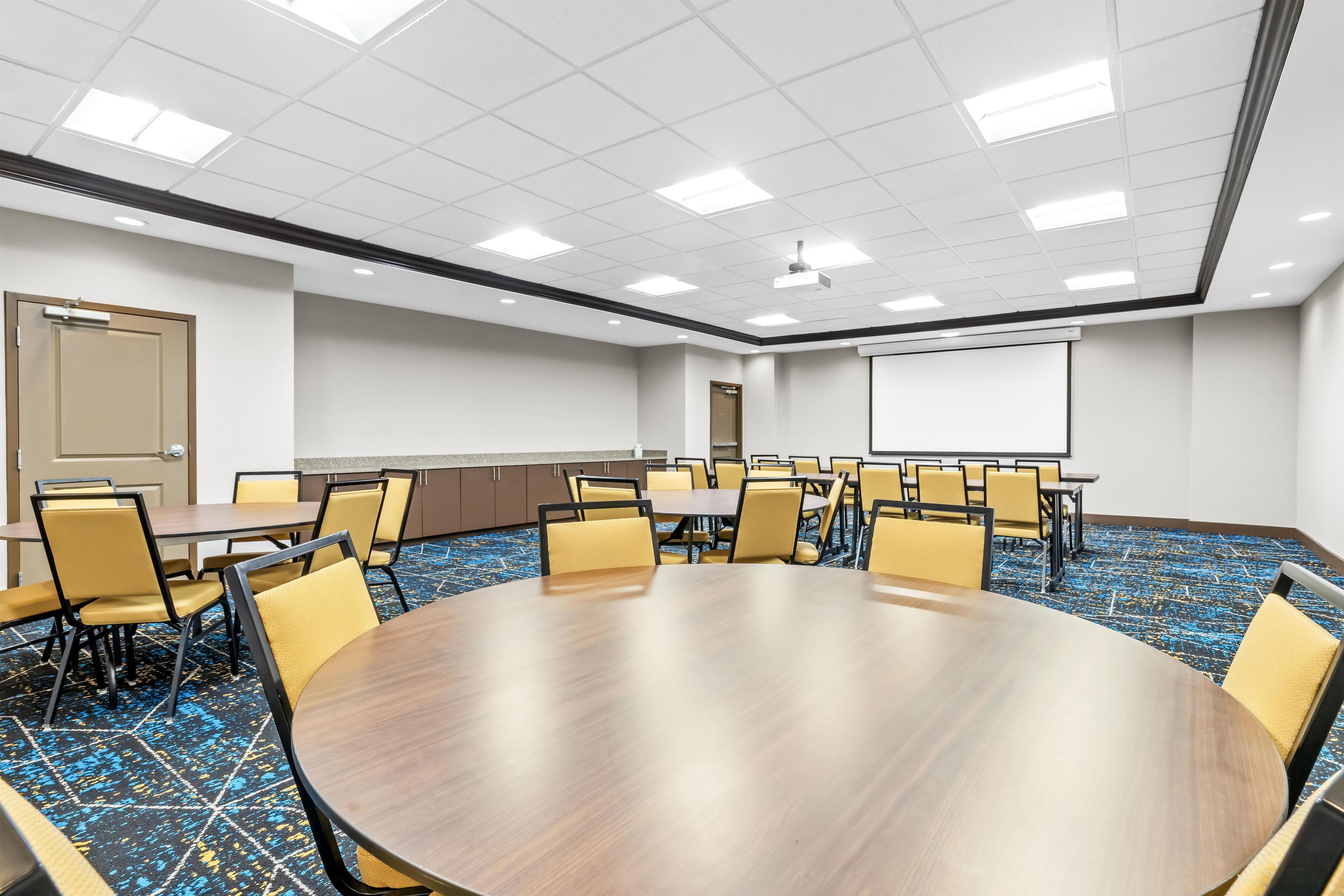 A conference room with a large oval table surrounded by chairs, a projector screen, and a door.