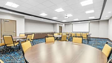 A conference room with a large oval table surrounded by chairs, a projector screen, and a door.