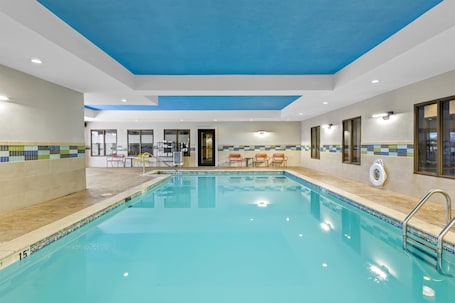 An indoor swimming pool with clear blue water, tiled walls, and a ceiling with a blue accent.