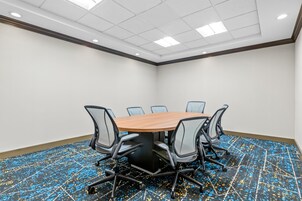 Un salón de conferencias con una mesa redonda, seis sillas y piso alfombrado.