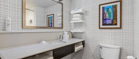 Un baño moderno con un espejo grande, un lavamanos blanco, un inodoro y una fotografía enmarcadas de un paisaje urbano en la pared.