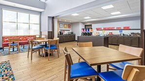 Un espace de restauration moderne avec des tables et des chaises en bois, une cuisine en arrière-plan et de grandes fenêtres.