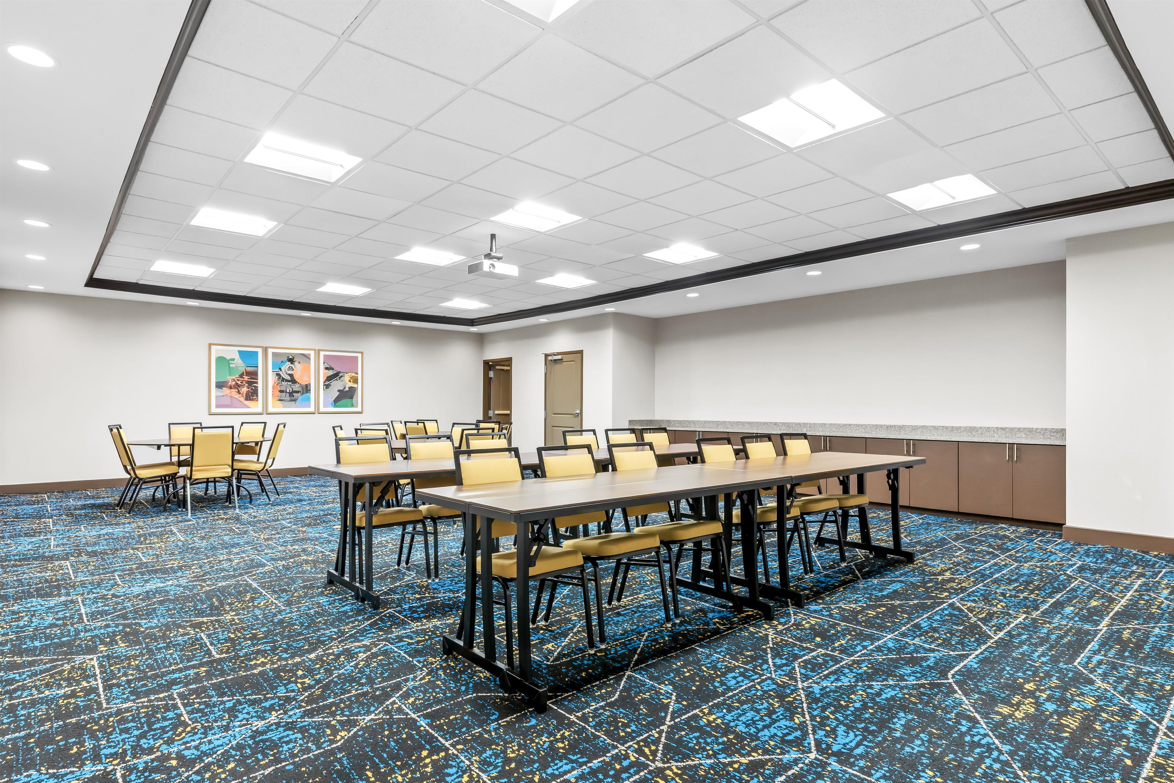 A conference room with a long table and chairs, a projector, and a carpeted floor.