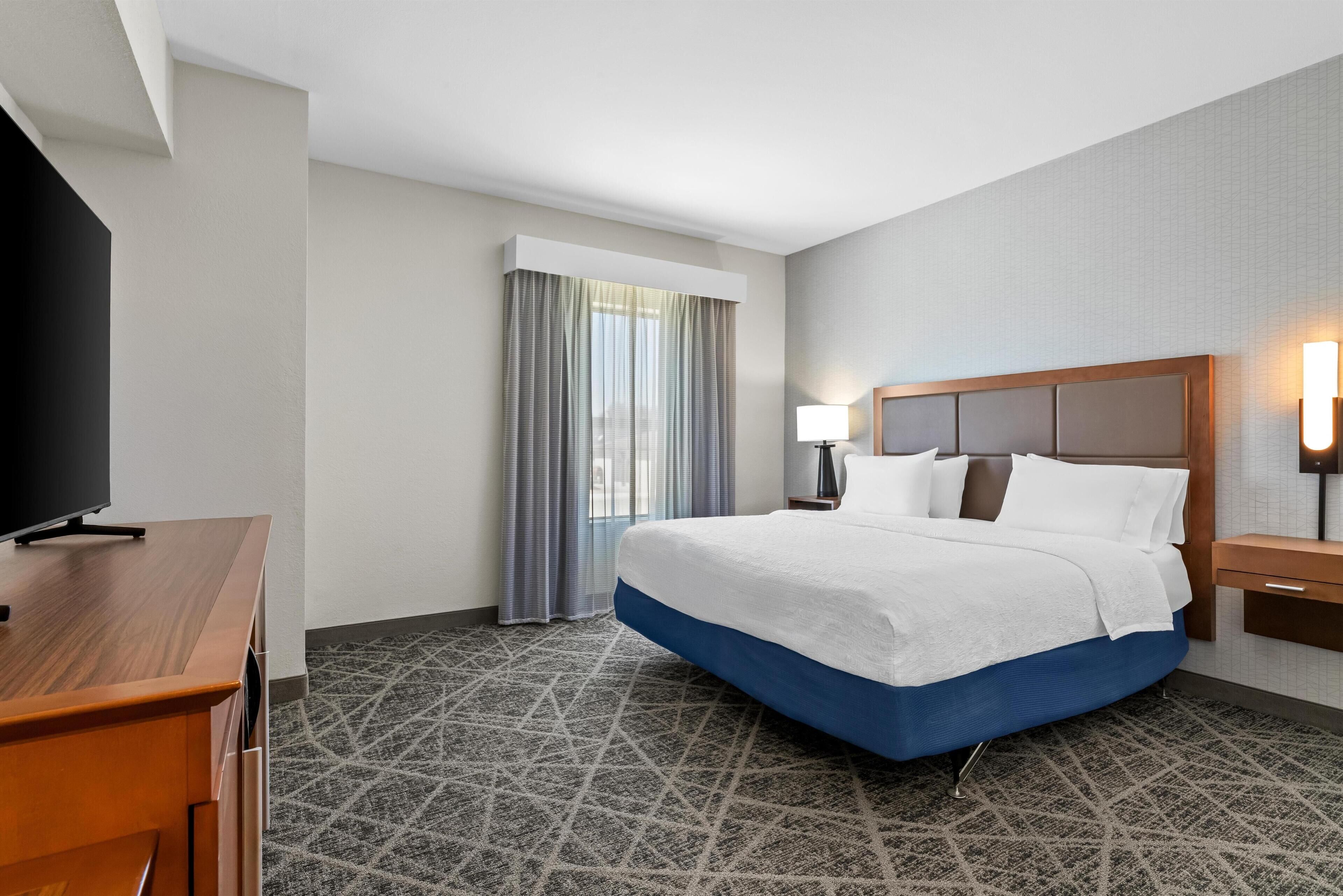 Une chambre d’hôtel avec un lit, une télévision, un bureau, une lampe et une fenêtre avec des rideaux.