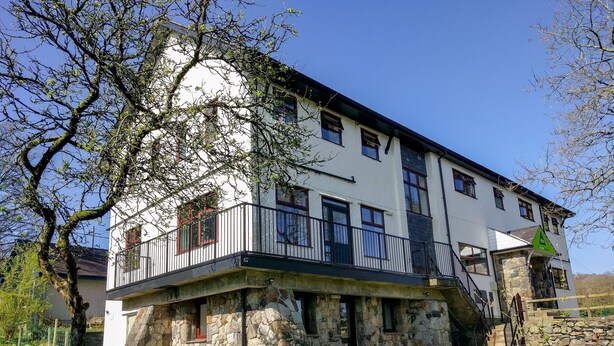 A two-story stone building with a balcony, a stone staircase, and a small garden area.