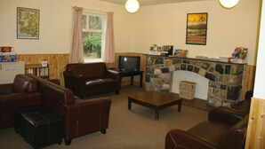A living room with leather sofas, a television, a stone fireplace, and a window with curtains. - YHA Snowdon Llanberis - Hostel (Caernarfon)