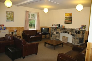 A living room with leather sofas, a television, a stone fireplace, and a window with curtains. - YHA Snowdon Llanberis - Hostel (Caernarfon)