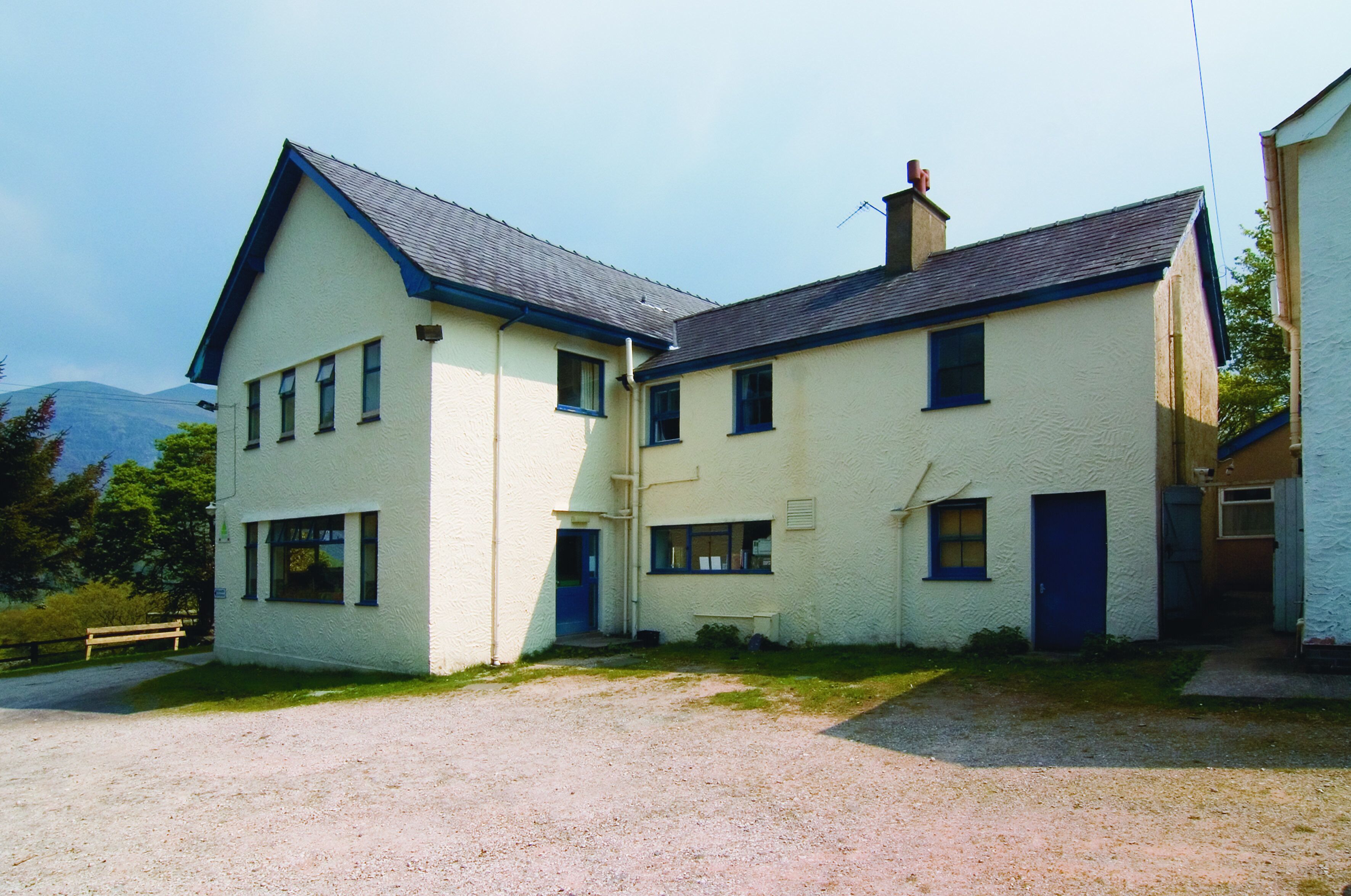 A two-story building with a gravel driveway and a bench.