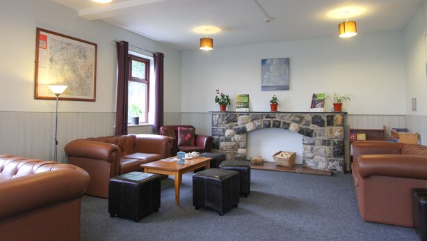 A cozy living room with leather sofas, a stone fireplace, and a map on the wall. - YHA Snowdon Llanberis - Hostel (Caernarfon)