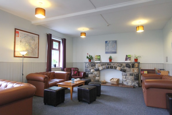 A cozy living room with leather sofas, a stone fireplace, and a map on the wall. - YHA Snowdon Llanberis - Hostel (Caernarfon)