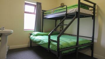 A bunk bed with green bedding in a room with a window and a sink.