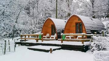 Deux cabanes en bois aux toits en arc, entourées d’arbres couverts de neige.