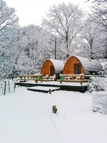 Duas cabanas de madeira com telhados arqueados, rodeadas por árvores cobertas de neve.