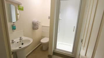 Un baño con lavamanos, inodoro y cabina de ducha con mampara de vidrio.