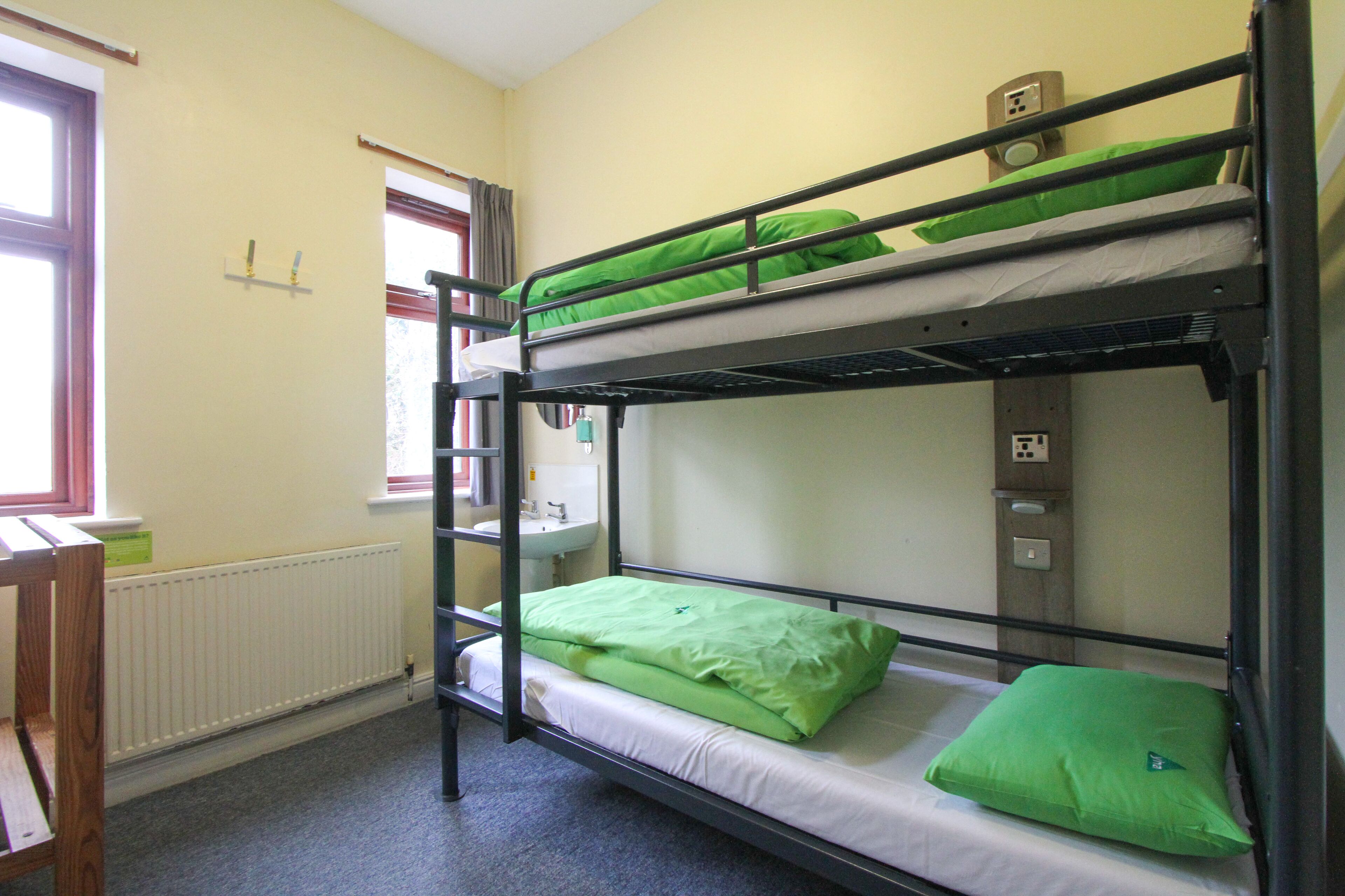 A bunk bed room with a window, radiator, and a small desk.